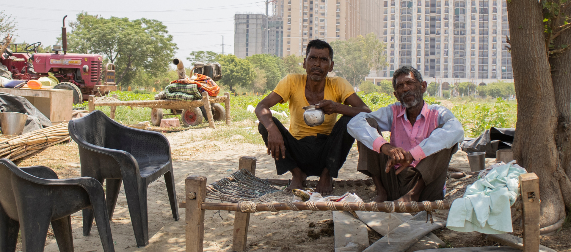 The image shows two men sitting under a tree to get respite from the heat in India.