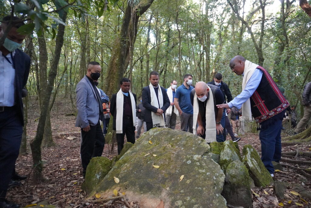The photo shows Tambor Lyngdoh and other community members observing an altar inside the forest.
