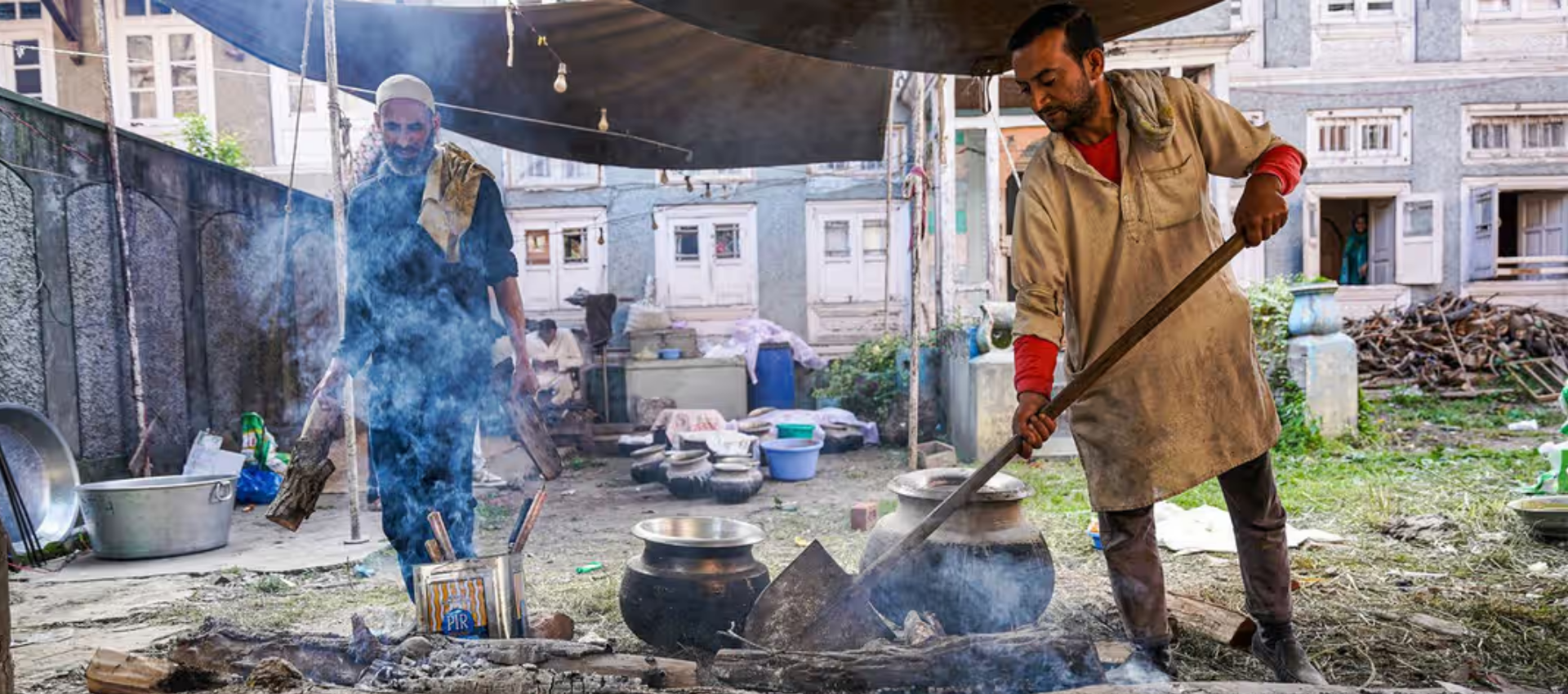 The image shows two men cooking food for a wedding in Kashmir.