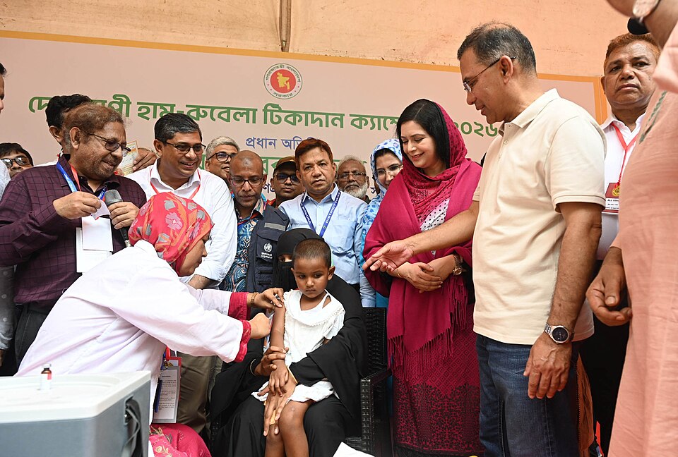 The image is a representational one and shows a child being vaccinated by a doctor, while the Bangladeshi Prime Minister could be seen on the right side of the frame.