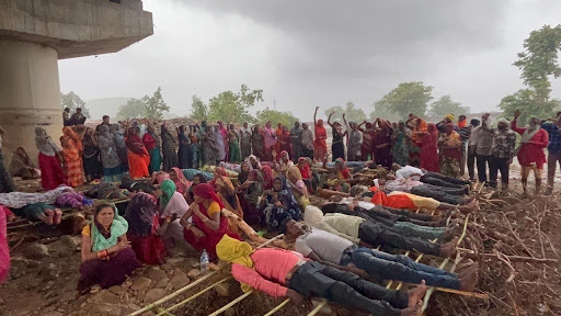 तस्वीर में कुछ पुरुषों को ज़मीन पर लेटे हुए दिखाया गया है, जबकि बैकग्राउंड में महिलाओं को बैठे हुए देखा जा सकता है।