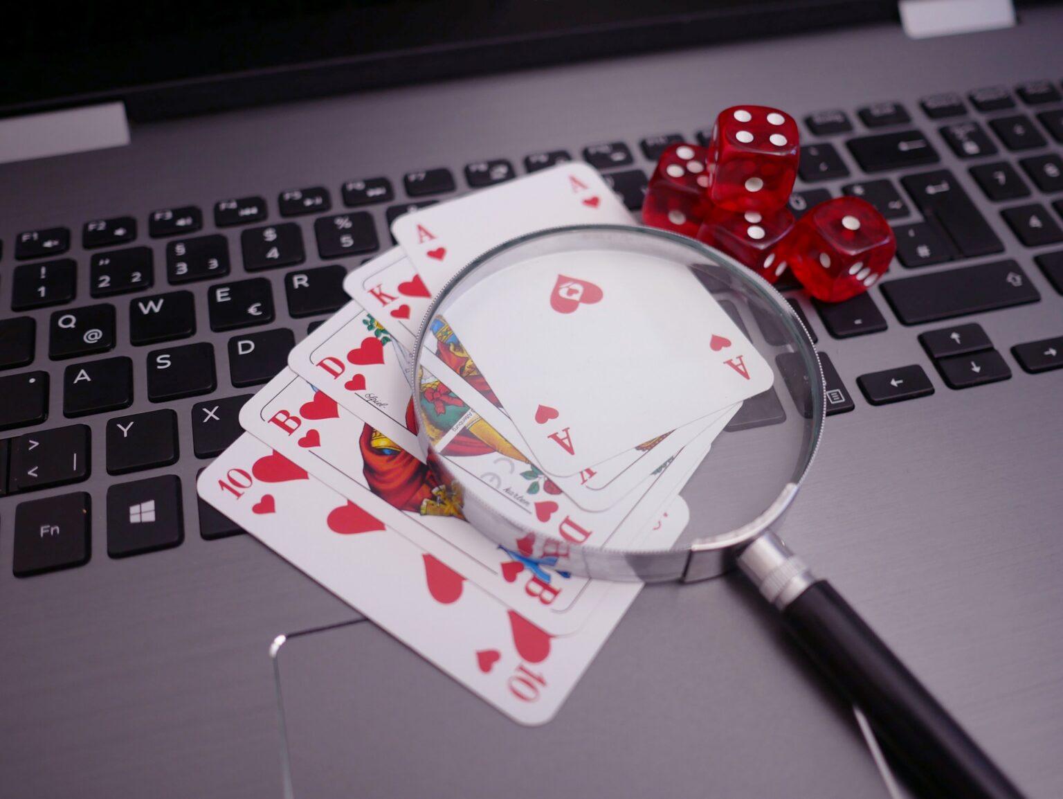The image shows a magnifying glass placed on playing cards that are laid out on a laptop.