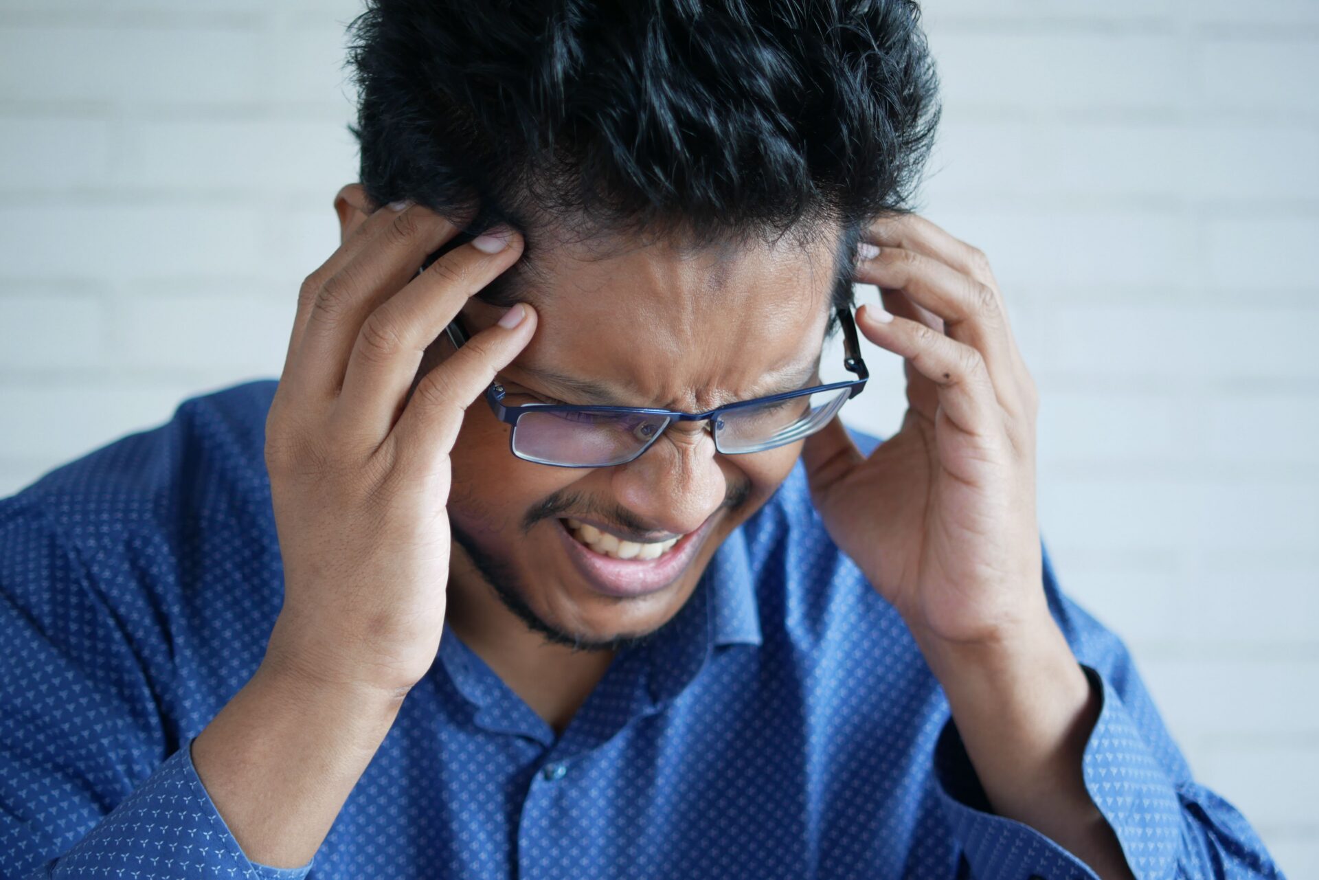 A man dressed in blue shirt is seen holding his head, aiming to show his frustration with headache.