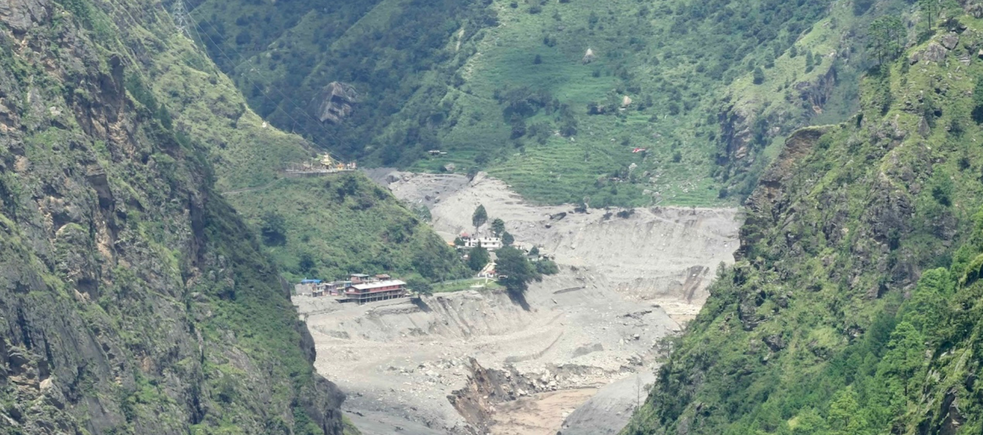 A landslide cuts through a green mountain valley in Nepal. Few houses could also be seen along the valley.