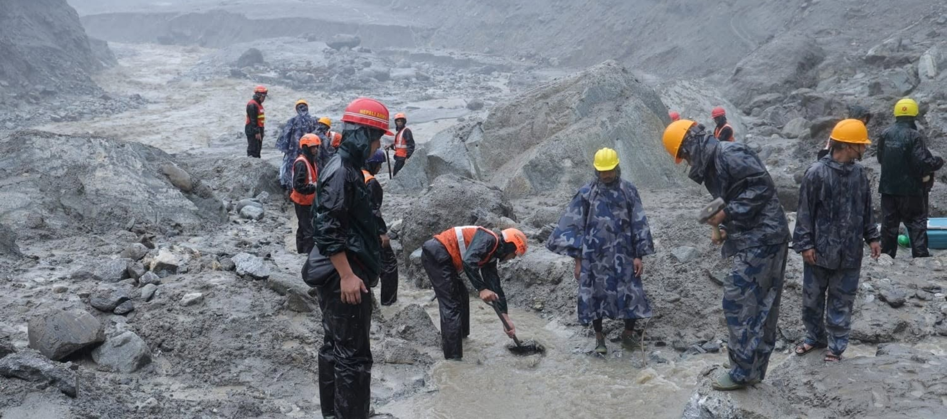 Rescue workers in gears and helmets search through mud, rocks, and debris in Nepal.
