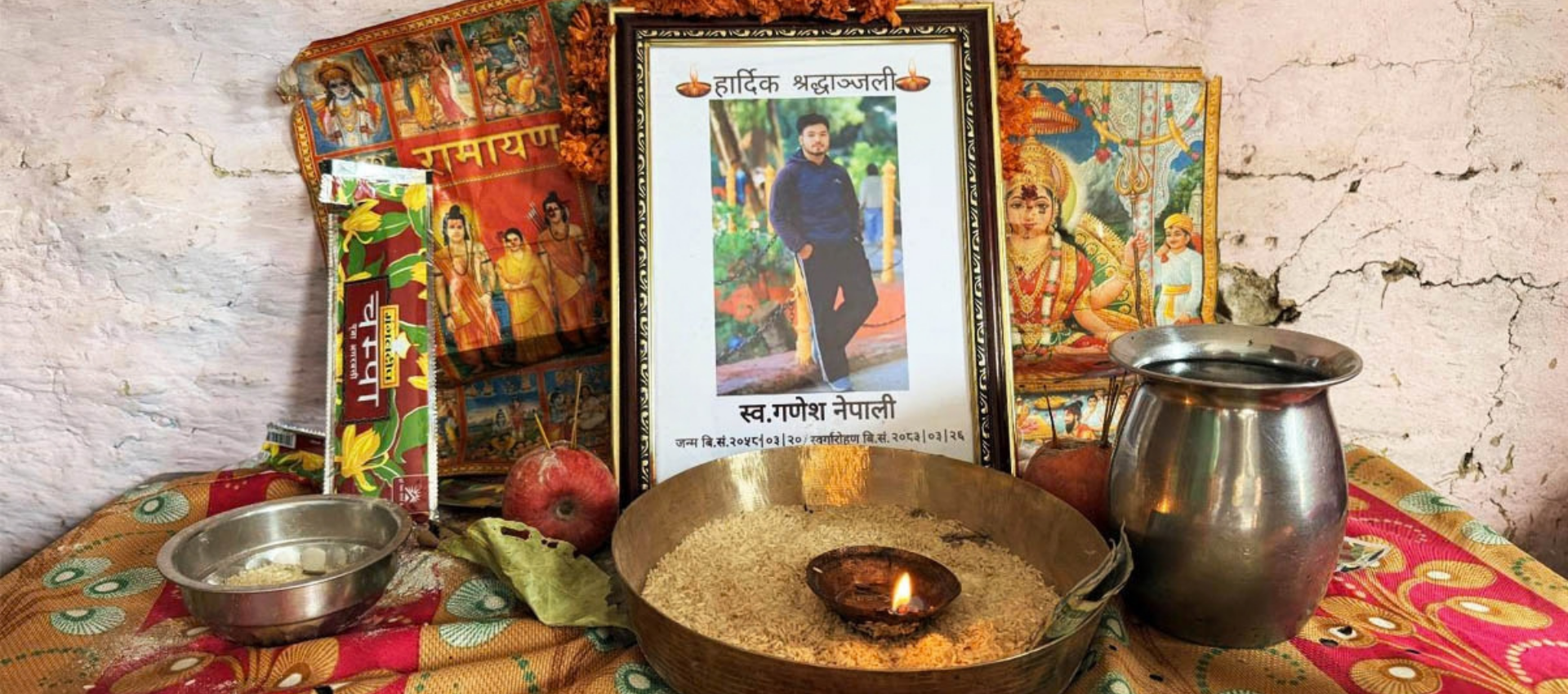 A framed photograph of a young man with a Hindi condolence message could be seen on a table placed inside a rented home in Nepal. Oil lamp and metal vessels are also seen next to the photo frame.