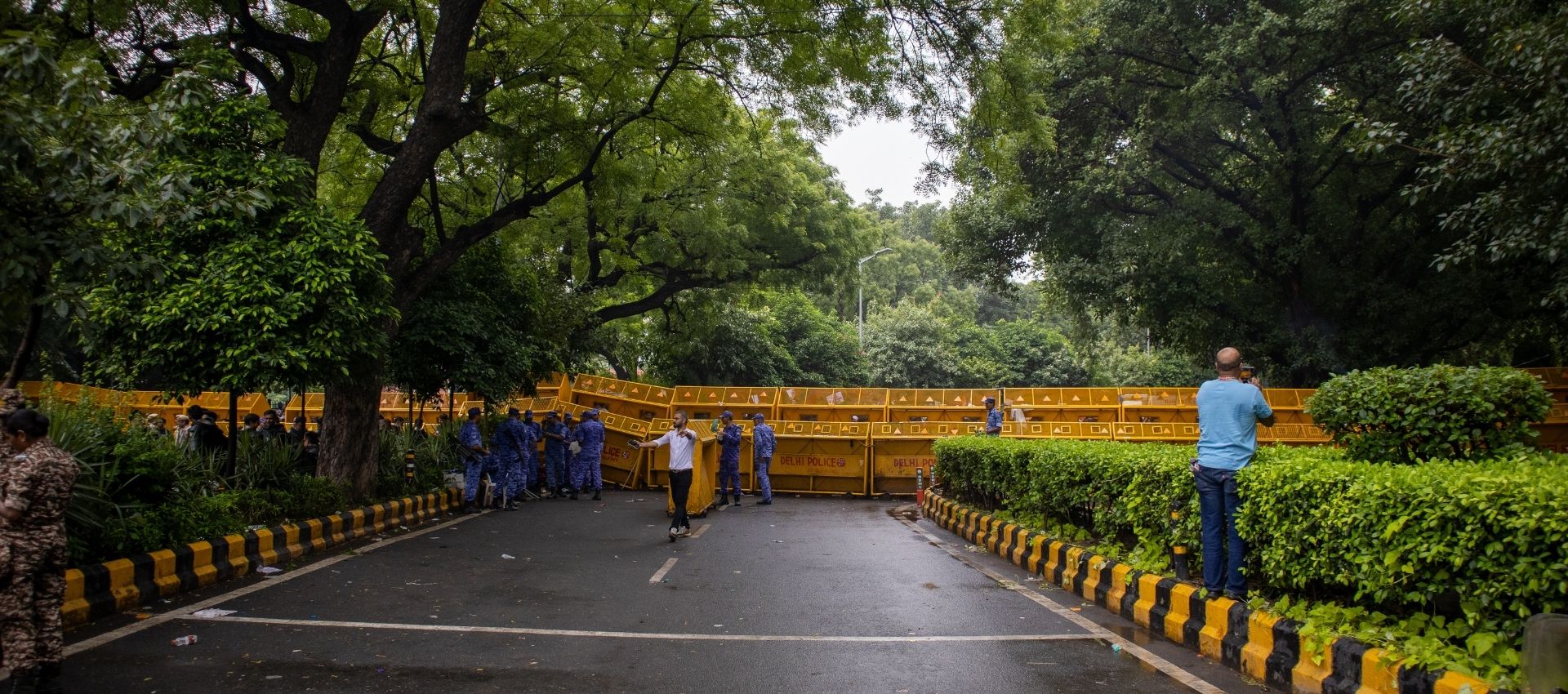 A road is blocked by yellow Delhi Police barricades, with several security personnel gathered near the center.