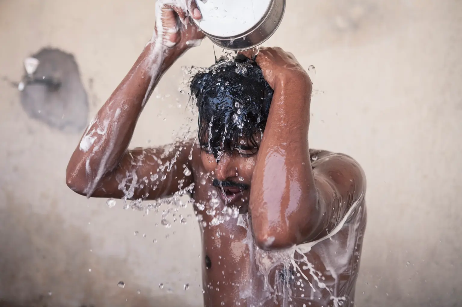 This is an image of a migrant construction worker from Nepal. The migrant is bathing in an open washroom at a workers' camp in Qatar.